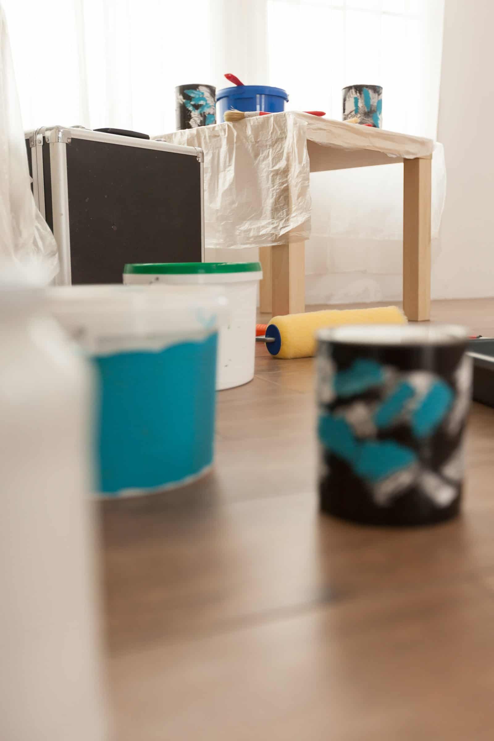 Paint supplies and tools for interior wall painting at home, including paint cans, brushes, roller, and protective coverings, prepared by Central Coast Painter Corp for painting projects.