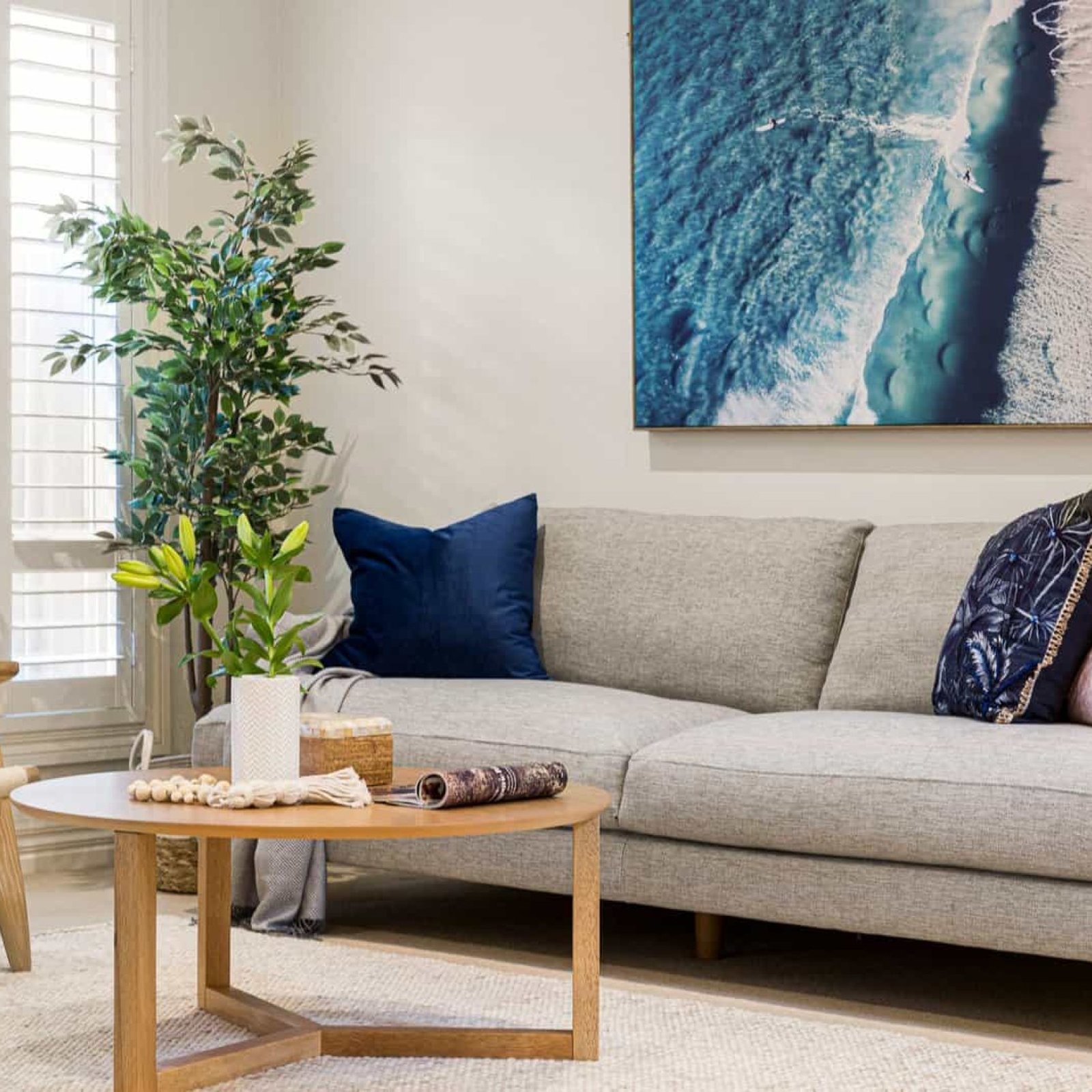 Vibrant seaside-inspired living room with coastal decor, large ocean artwork, neutral sofa with colorful pillows, indoor plants, and natural light for a relaxing coastal ambiance.