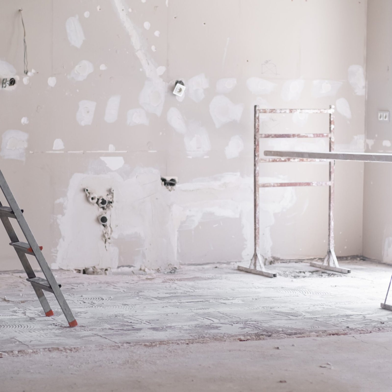 Ladder and construction equipment standing in empty room illuminated by bright sunlight shabby wall with holes and stains ready for painting renovation process in apartment